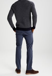 Pull en maille bleu marine à pois blancs, associé à un pantalon chino bleu marine et des bottines en daim marron. Le look présente un design texturé.