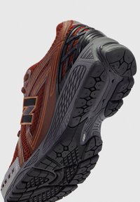 Scarpe sportive rosse e grigie con tomaia in rete, suola in gomma testurizzata e un pattern di tread prominente. Presenta un logo nero sul lato.