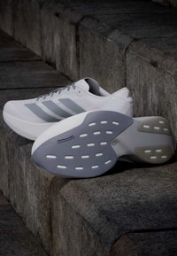 Ζευγάρι λευκά και γκρι παπούτσια Adidas για τρέξιμο σε πέτρινα σκαλοπάτια, ένα παπούτσι δείχνει την σόλα με σήμανση Continental.