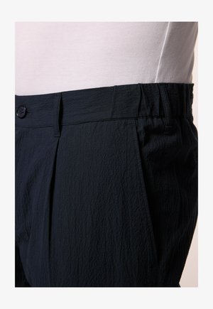 Marineblauwe broek van textuurstof, met een geplooide voorkant en een knoopsluiting bij de tailleband. Details van een elastische tailleband zichtbaar.