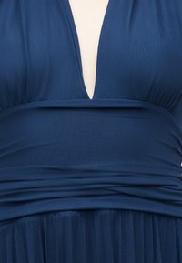 Dybtblå kjole med V-udskæring, tilpasset talje og plisseret nederdel.
