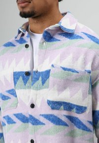 Fleece shirt met een paars, blauw en groen zigzag-patroon. Voorzijde met knopen, een borstzak en een klassieke kraag.
