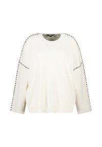 Witte ribgebreide trui met zwarte gestikte details langs de schouders en mouwen, voorzien van een ronde halslijn en lange mouwen.