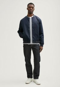 Chaqueta bomber navy, camiseta de rayas, jeans oscuros, zapatillas blancas. La chaqueta cuenta con botones y puños de canalé, la camiseta tiene rayas horizontales.