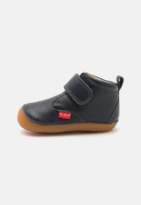 Botte en cuir bleu marine avec une sangle en Velcro, semelle en caoutchouc marron et détails de couture. Étiquette Kickers rouge cousue sur le côté. Design à bout rond.