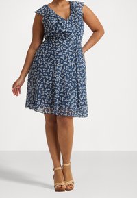 Floral wrap dress in navy blue with white patterns. Features ruffled neckline and shoulder straps, flowing fabric, and a knee-length hem.