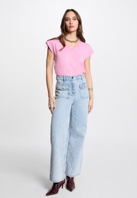 Maglietta rosa a maniche corte con scollatura a V abbinata a jeans a vita alta blu chiaro e a gamba larga. Tacchi a punta bordeaux lucidi. Dettagli in gioielleria argentata.