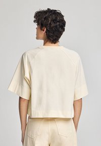 Krämfärgad croppad t-shirt med korta raglanärmar, tillverkad av mjuk bomull. Minimalistisk design med en enkel yta och utan synliga dekorationer.