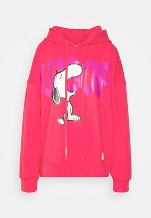 Henkilö pukeutunut punaiseen Snoopy-huppariin, mustaan nahkaminihameeseen, mustiin korollisiin nauhallisiin saappaisiin ja pitää mustaa käsilaukkua harmaan seinän edessä.