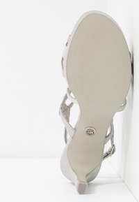 Chaussure argentée à talon haut avec bout ouvert, surface texturée et brides autour de la cheville. Dispose d'une semelle en caoutchouc avec un logo subtil et une taille 37.