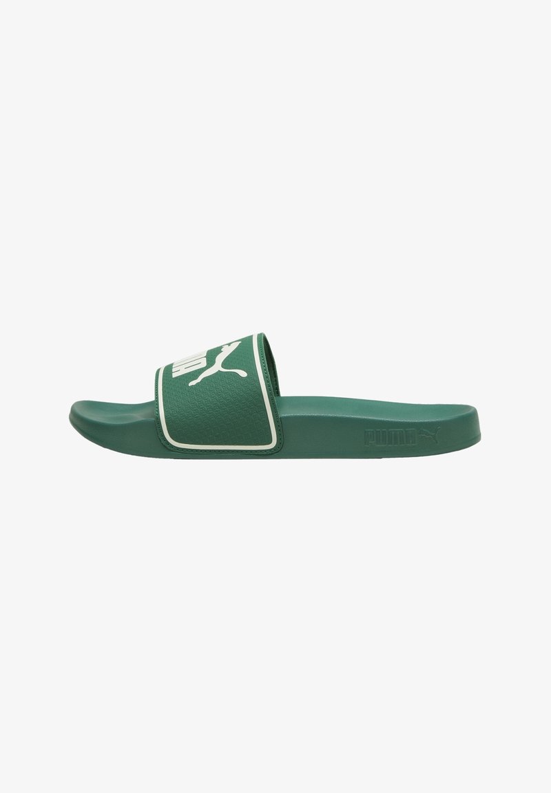 Sandale slide Puma verte avec logo blanc sur une large bride et une semelle texturée, vue de côté sur fond blanc.