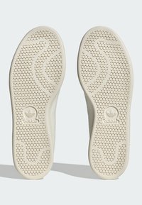 Hvide gummisko såler med teksturerede, runde mønstre. Har et bølget design og Adidas-logoet på den ydre hæl.