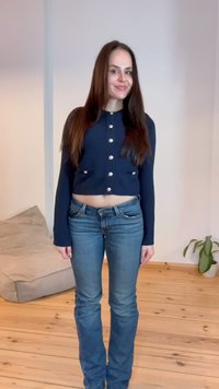 Mornarsko pleteno cardigan z gumbnimi detajli, skrajšane dolžine in dolgimi rokavi. Ujemajoč se z oprijetimi, svetlo modrimi kavbojkami. Enostavna ozadje.