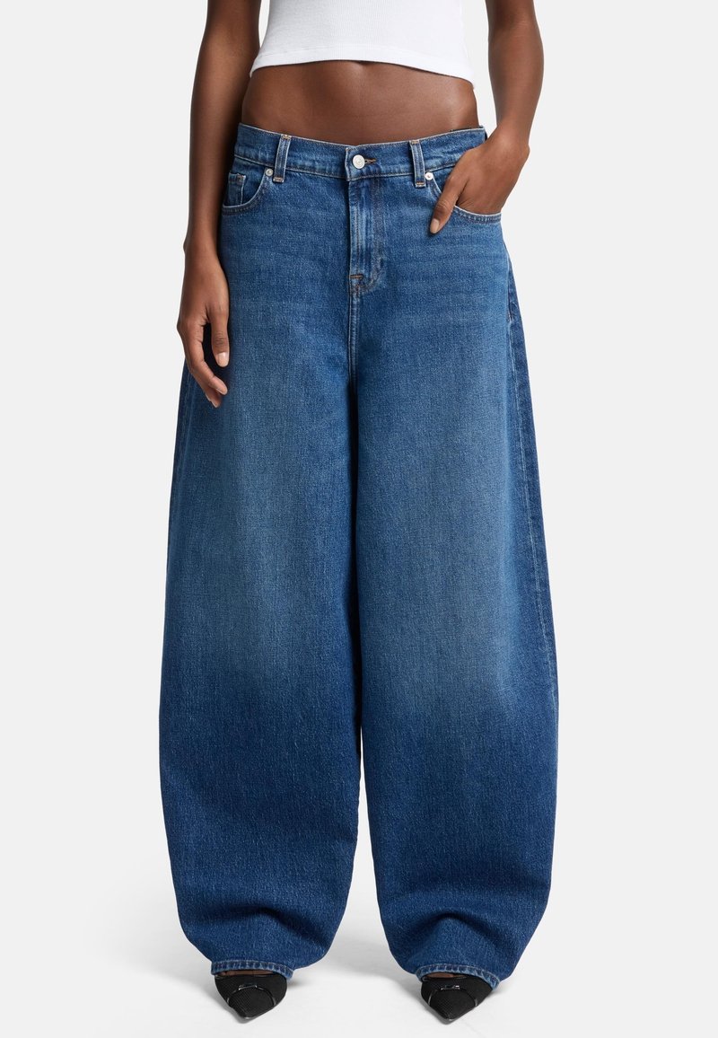 Jeans in denim blu oversized con un design a gamba larga, vita alta e cuciture visibili. Tessuto texturizzato con una finitura classica in lavaggio sbiadito.
