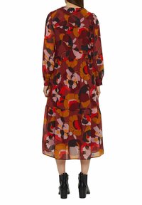 Lång blommig klänning med lagerdesign i nyanser av röd, orange och rosa. Genomskinligt tyg med långa ärmar och en tierad fåll. Svarta ankelstövlar.