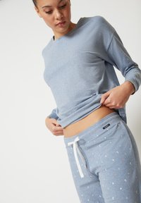 Hellblaues Langarmshirt aus weichem Stoff, kombiniert mit passenden Jogginghosen, die über einen weißen Kordelzug und kleine Stern- und Mondmuster verfügen.