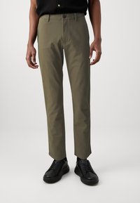 Chinos vert olive à coupe droite, en coton, avec poches avant et fermeture à un seul bouton. Associés à des baskets noires.