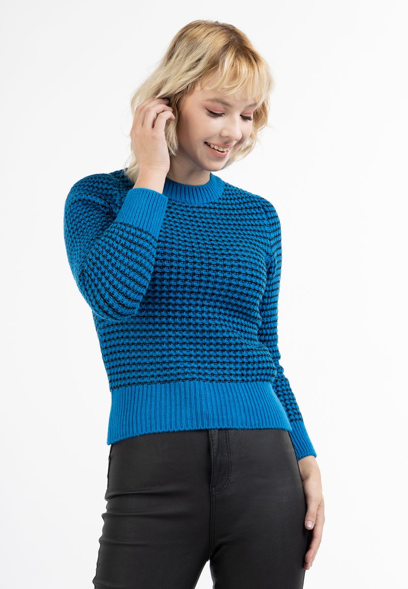 Pulover tricotat albastru cu model texturat, manșete și tiv din bumbac ribbed, guler rotund și design ajustat, purtat cu pantaloni negri.