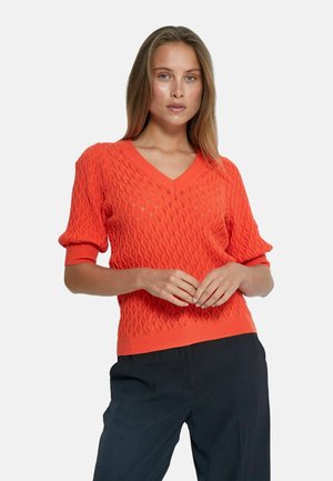V-neck, short-sleeve pullover in bright orange, featuring a textured wave pattern; paired with black trousers.