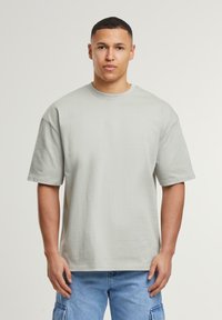 Lysegrå oversized t-shirt lavet af bomuld, med rund hals og korte ærmer, præsenteret mod en neutral baggrund.