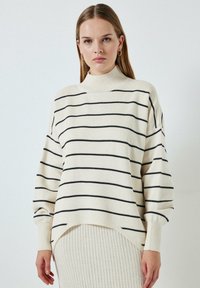 Kreemist soonest kudum, millel on mustad horisontaalsed triibud, kõrge kaelus, langenud õlad ja ribakudumiga mansetid. Omab asümmeetrilist hemline'i.