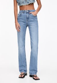 Jeans en denim bleu clair avec une taille haute et une coupe droite, dotés de cinq poches et d'une fermeture classique par bouton et fermeture éclair.