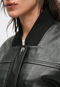 Veste en cuir noire avec col côtelé noir, dotée d'une fermeture à boutons-pression et de détails de couture sur la poitrine.