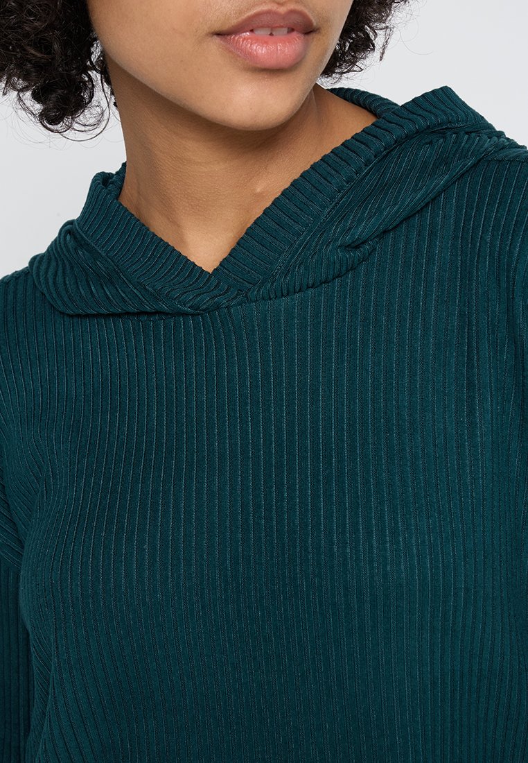 Sudadera de canalé en color azul verdoso con diseño de cuello de cisne. La tela tiene una textura suave, con líneas verticales y un ajuste holgado.