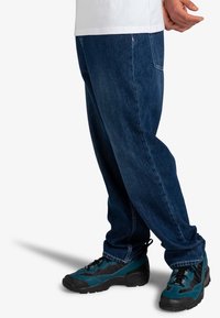 Jean en denim bleu foncé, coupe décontractée avec des jambes droites ; associé à des chaussures de randonnée bleu sarcelle et noires avec des accents texturés et des lacets.