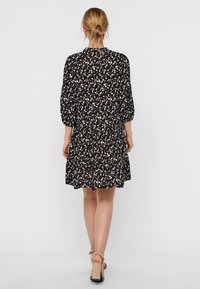 Schwarzes Kleid mit floralem Muster, ausgestattet mit 3/4-Puffärmeln, einem runden Ausschnitt und einem ausgestellten Rock. Leichter Stoff mit weicher Textur.
