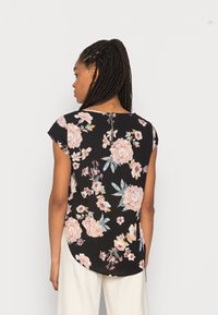 Top com padrão floral apresentando um fundo preto com flores rosas e azuis, mangas curtas e uma bainha arredondada. A parte de trás tem um detalhe em forma de buraco de fechadura.