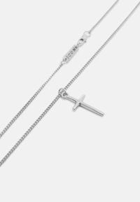 Collar de cadena de plata con un pequeño colgante en forma de cruz y un cierre que incluye una plaquita rectangular grabada con texto.