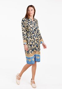 Vestido de leopardo en beige y negro, con acentos en azul y un dobladillo estampado. Las mangas largas y el diseño de escote en V realzan su silueta.