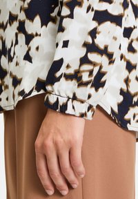 Langärmeliges Hemd mit weißem und marineblauem abstraktem Blumenmuster und braunen Akzenten; weicher Stoff mit gerafftem Manschettendetail.