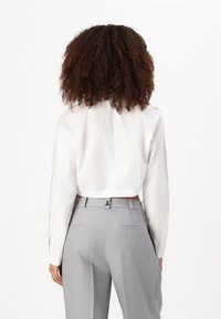 Camicia bianca a maniche lunghe con colletto, con dettaglio della cucitura posteriore, abbinata a pantaloni grigi su misura con tasche e passanti per la cintura.