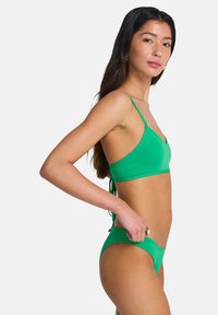 Σετ πράσινου μαγιό μπικίνι με τριγωνικό τοπ και λεπτές ρυθμιζόμενες τιράντες, καθώς και ταίριασμα με εσώρουχα χαμηλής μέσης. Λείο, ελαστικό υλικό με μίνιμαλ σχεδίαση.