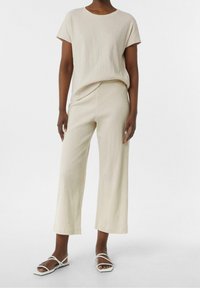 Top beige texturizado con mangas cortas, combinado con pantalones de pierna ancha a juego. Acentuado con sencillas sandalias planas blancas.