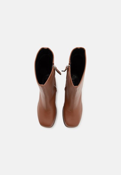 Bottes en cuir marron montantes avec une texture lisse, bout carré et fermeture éclair sur le côté. L'intérieur est noir.