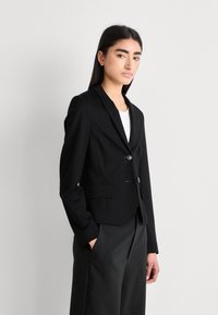 Musta räätälöity bleiseri, jossa on slim fit -leikkaus, yksinäinen nappisulku, viisteet lapelit ja sivutaskut. Sujuva kangas, jossa on jämäkkä muoto.