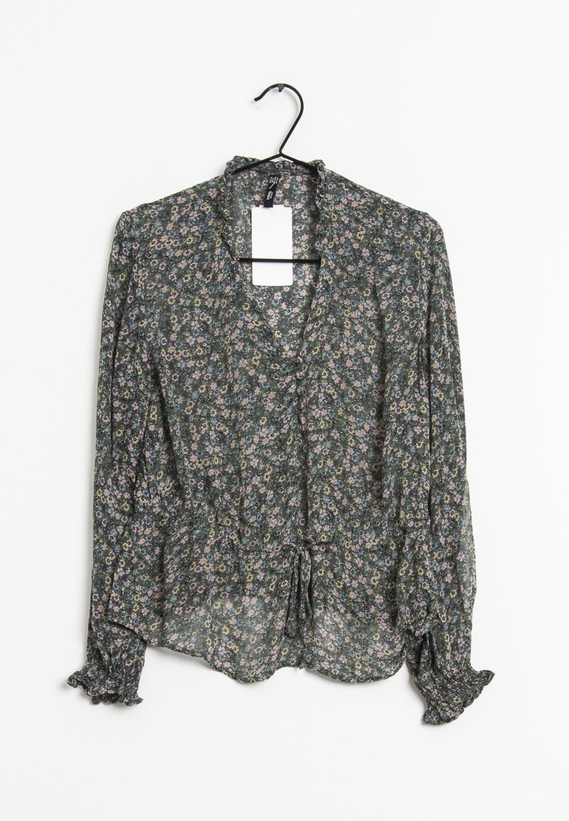 Blouse florale en tissu vert foncé, avec un ourlet noué à l'avant, des manches longues avec des poignets volants, et un motif de fleurs subtil en rose et jaune.