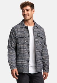 Plaid jacket in black and white with beige accents; features button closure and two front pockets; fabric appears textured and warm.