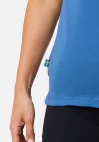 Blå bomullströja med rundad nederkant, som har en liten gul och blå svensk flagga som etikett på vänstra sidan nära sömmen.