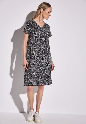 Navy blue short-sleeve dress with a wave pattern in cream, V-neck design, relaxed fit, and knee-length. Paired with white sneakers.