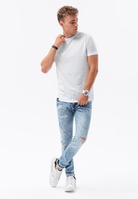 Vit bomulls t-shirt, figurnära design, matchad med ljusblå slitna jeans med revor. Modellen bär vita sneakers och en klocka.