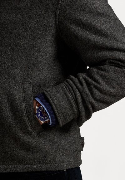 Dark gray wool jacket with a soft texture, featuring a front pocket. A blue watch partially visible under the cuff of a blue shirt.