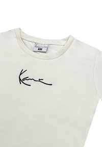 Witte katoenen T-shirt met korte mouwen en een ronde hals. Bevat een zwart geborduurd handtekening op de borst. Etiket toont maat XS.
