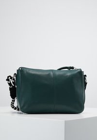Grön läder crossbody-väska med en slät textur, dragkedjestängning, justerbar rem med svart och vit randig accent.