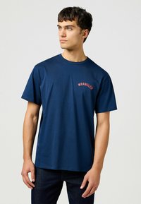 Tummansininen puuvillapaita, jossa on pyöreä kaula-aukko ja lyhyet hihat. Rinnassa on punaisella kirjaillut "WRANGLER". Sujuva pinta.