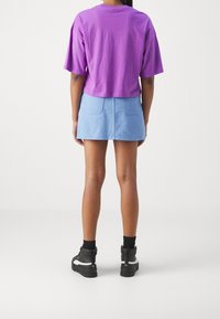 Fialové zkrácené tričko, světle modrá džínsová sukně se dvěma zadními kapsami, čern é vysoké tenisky s bílými akcenty a strukturovanou látkou.