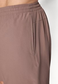 Hellbraune Shorts mit einem elastischen Bund und Seitentaschen. Der Stoff hat eine glatte Textur und einen lässigen Schnitt.